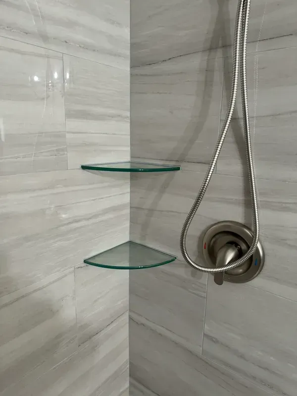 A shower with three glass shelves and a shower head.