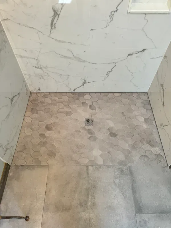 A walk in shower with a marble wall and tile floor.
