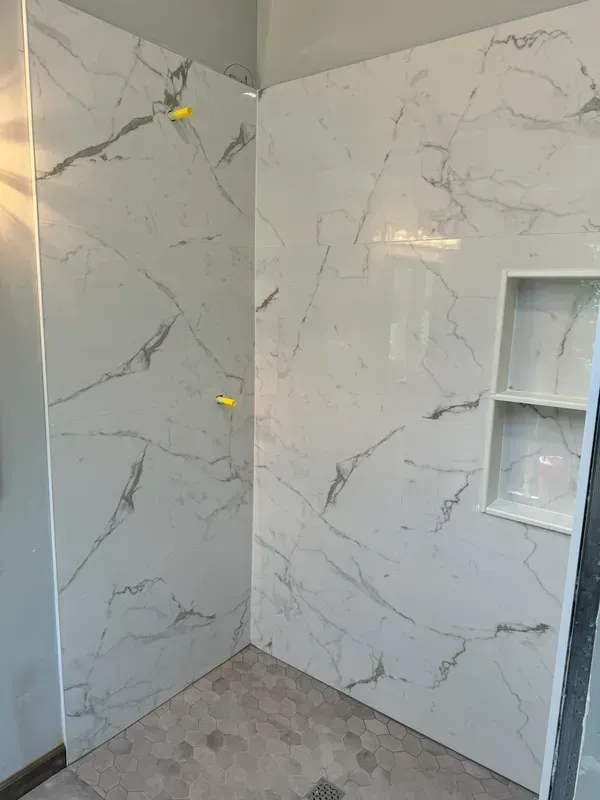 A bathroom with a shower stall and a marble wall.