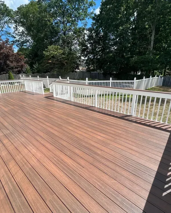 A large wooden deck with a white railing and trees in the background.
