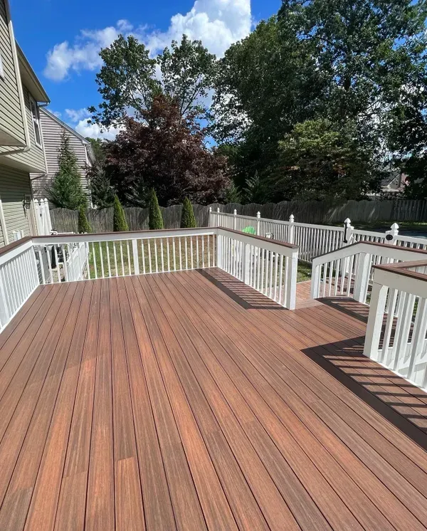 A large wooden deck with a white railing and trees in the background.