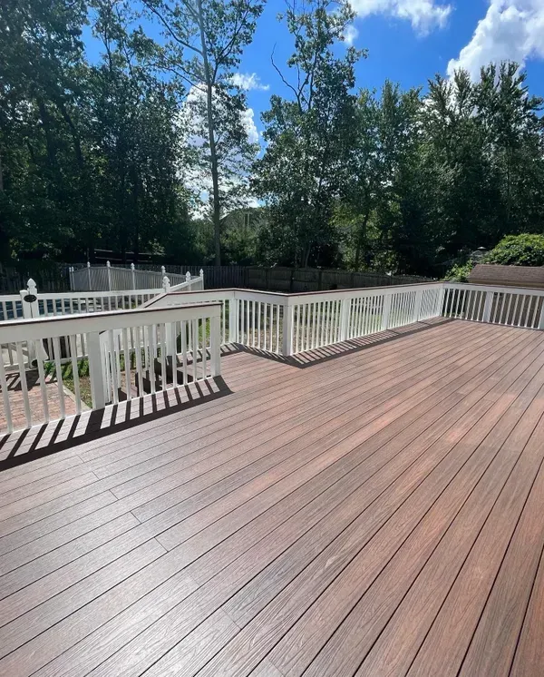 A large wooden deck with a white railing and trees in the background.
