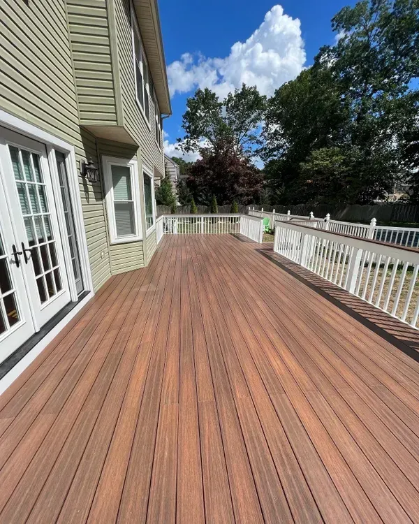 A large wooden deck with a white railing in front of a house.