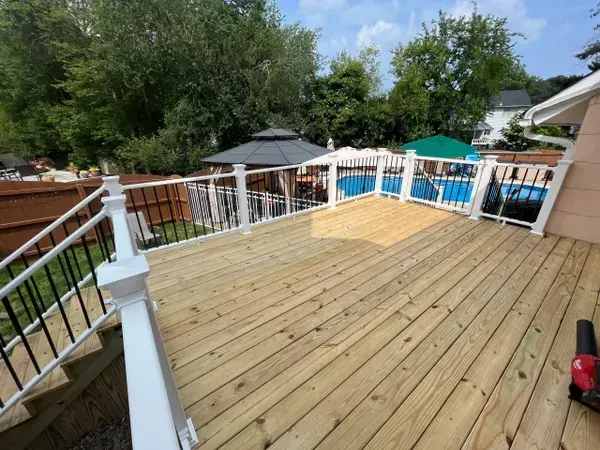 A wooden deck with a white railing and a pool in the background.