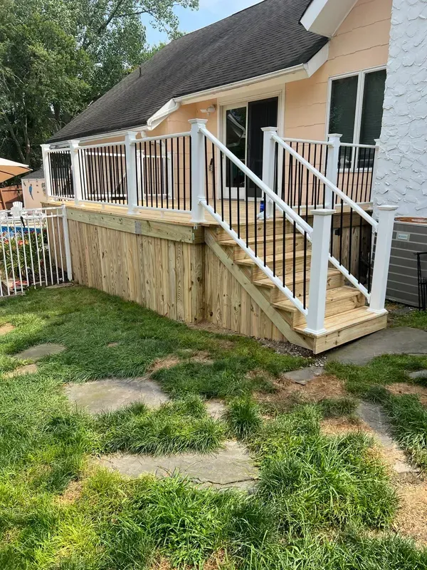 A wooden deck with stairs leading up to it is in the backyard of a house.