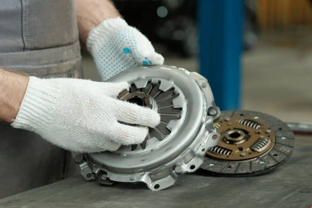 A mechanic wearing protective gloves holding a car clutch.
