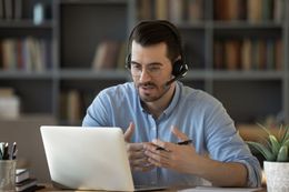 A man wearing headphones is sitting in front of a laptop computer.