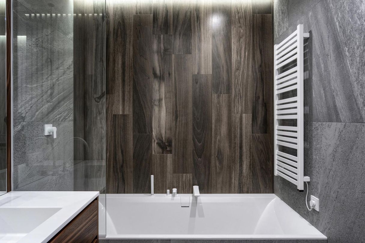 Bagno moderno con vasca bianca, parete in legno scuro e termoarredo bianco.