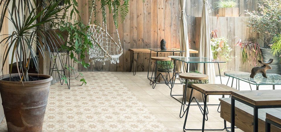 Luminoso patio interno soleggiato con piante in vaso, tavolini e sedie in vetro accanto a una finestra e pavimento decorato.