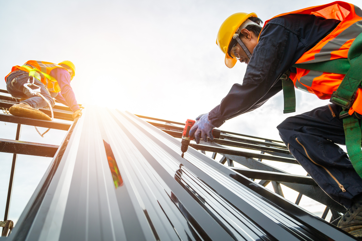 Construction workers installing metal roofing, wearing safety gear, on a building.