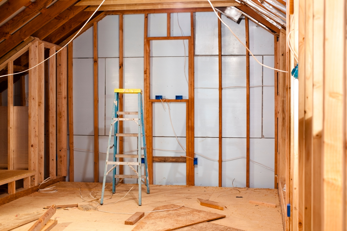 Interior view of a room under construction with wood framing, insulation, and a ladder.