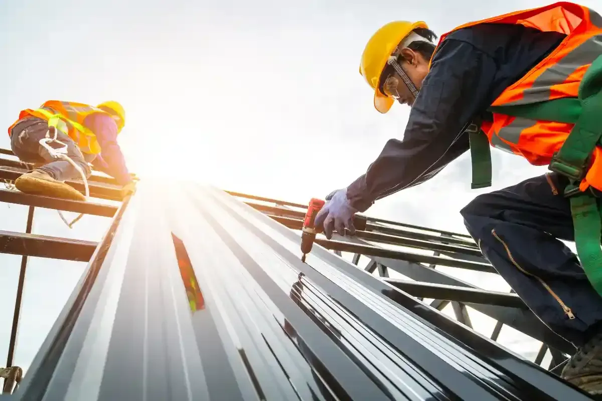 Construction workers installing metal roofing, wearing safety gear, on a building.