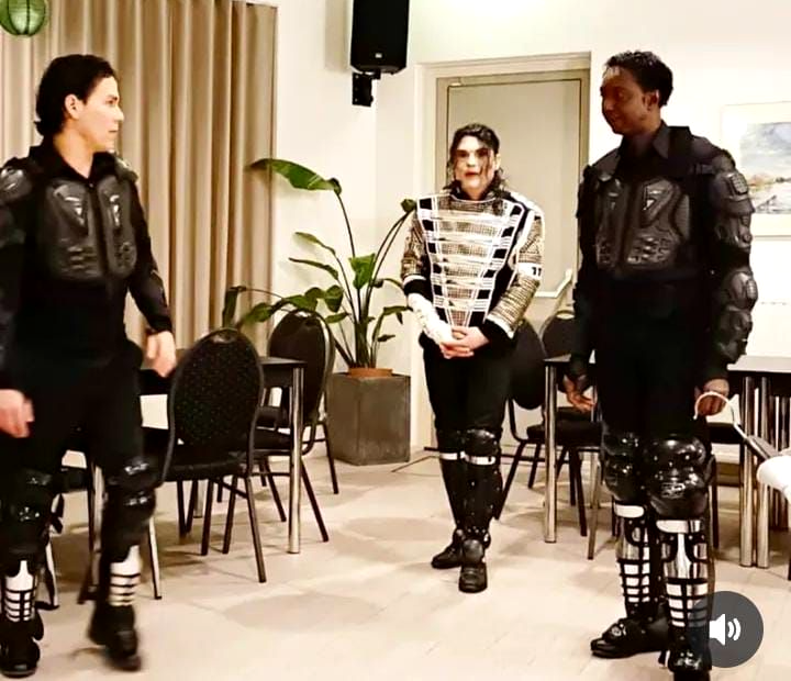 dutchmichaeljackson Drie artiesten staan op het podium en dansen in zwarte outfits met zilveren accenten, onder roze en rode podiumverlichting.