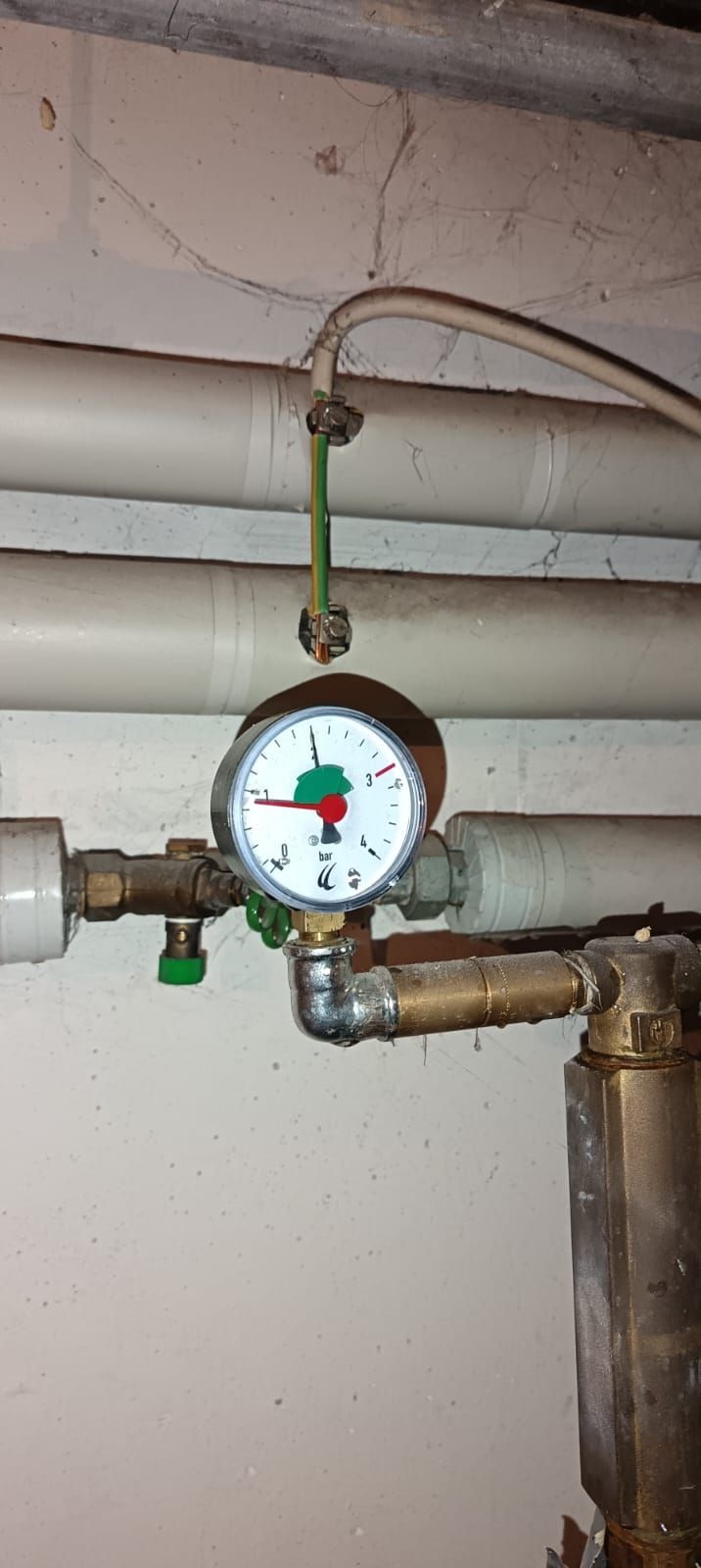 A pressure gauge is hanging from a pipe on a wall.