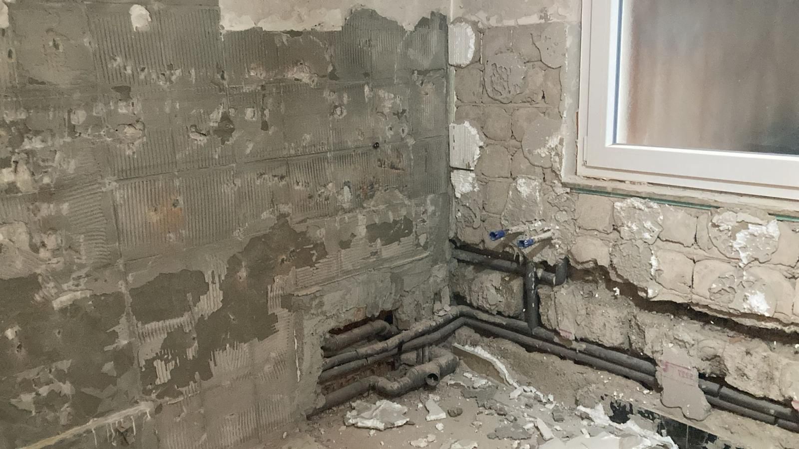 A bathroom under construction with pipes coming out of the wall and a window.