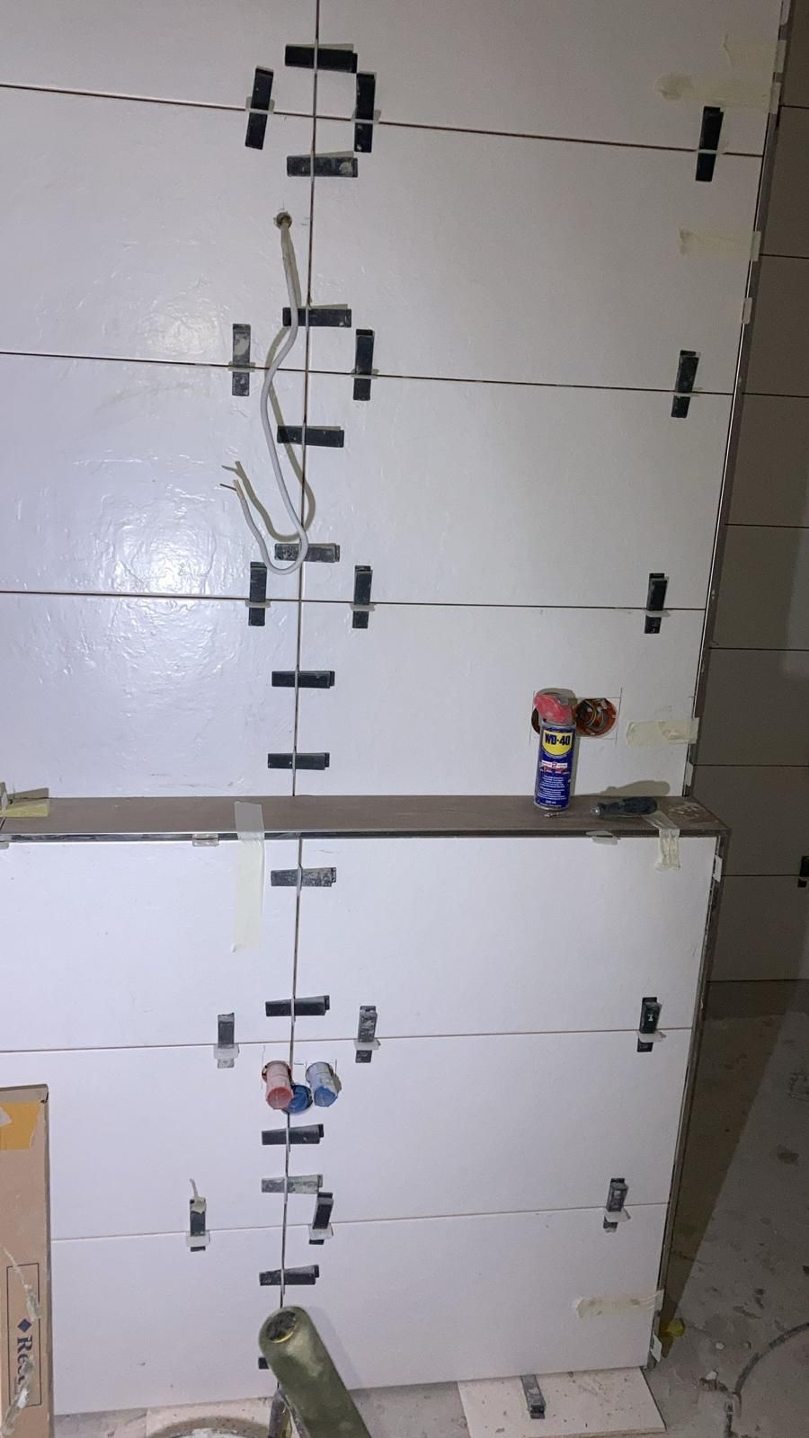 A row of white tiles are being installed on a wall.