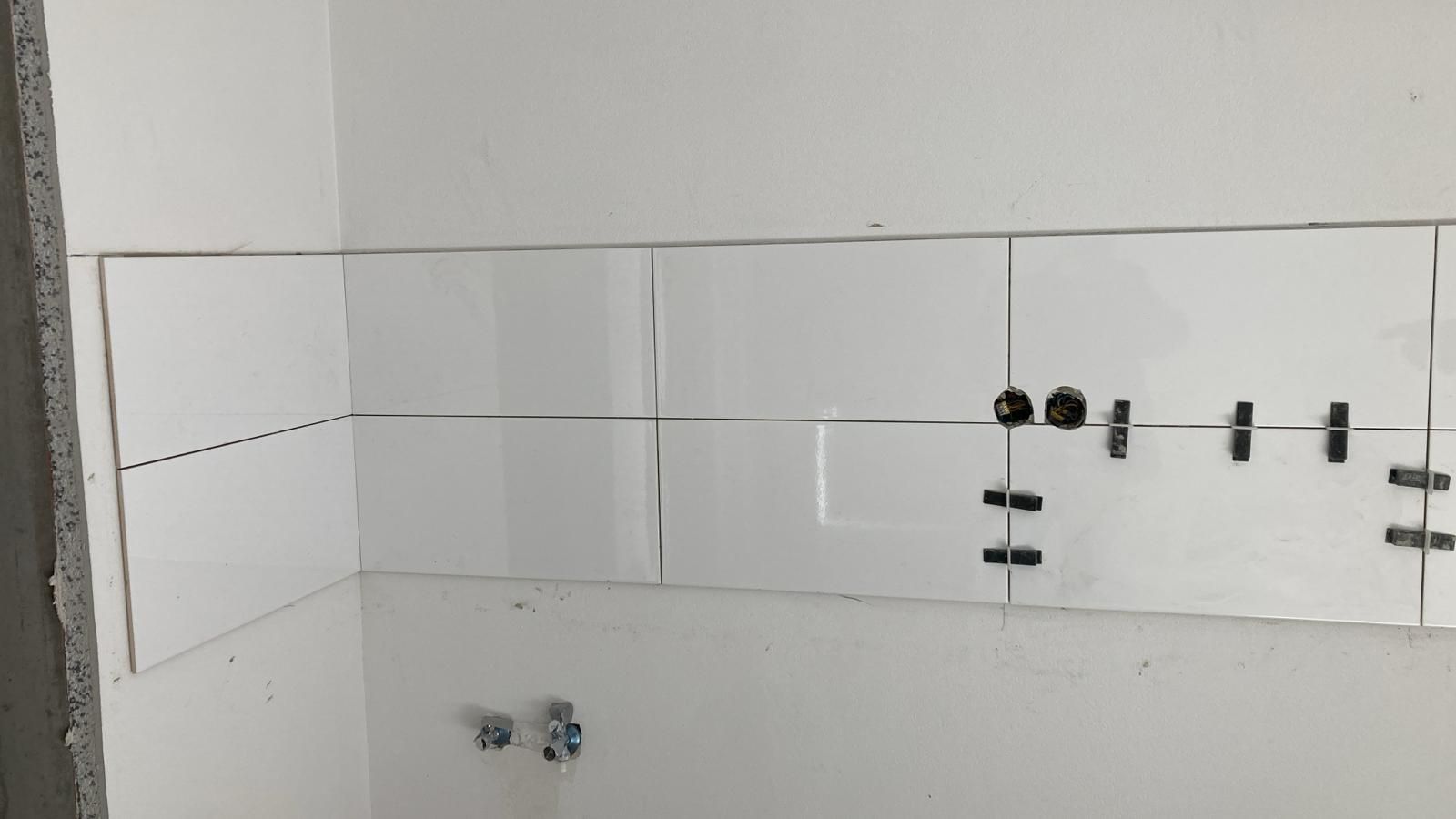 A bathroom with white tiles being installed on the wall.