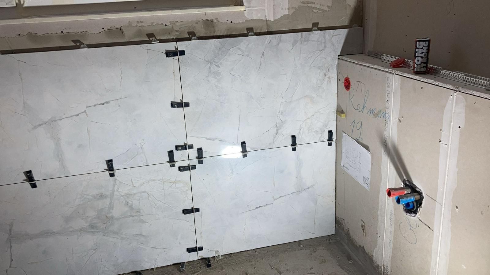 A bathroom under construction with tiles being installed on the wall.