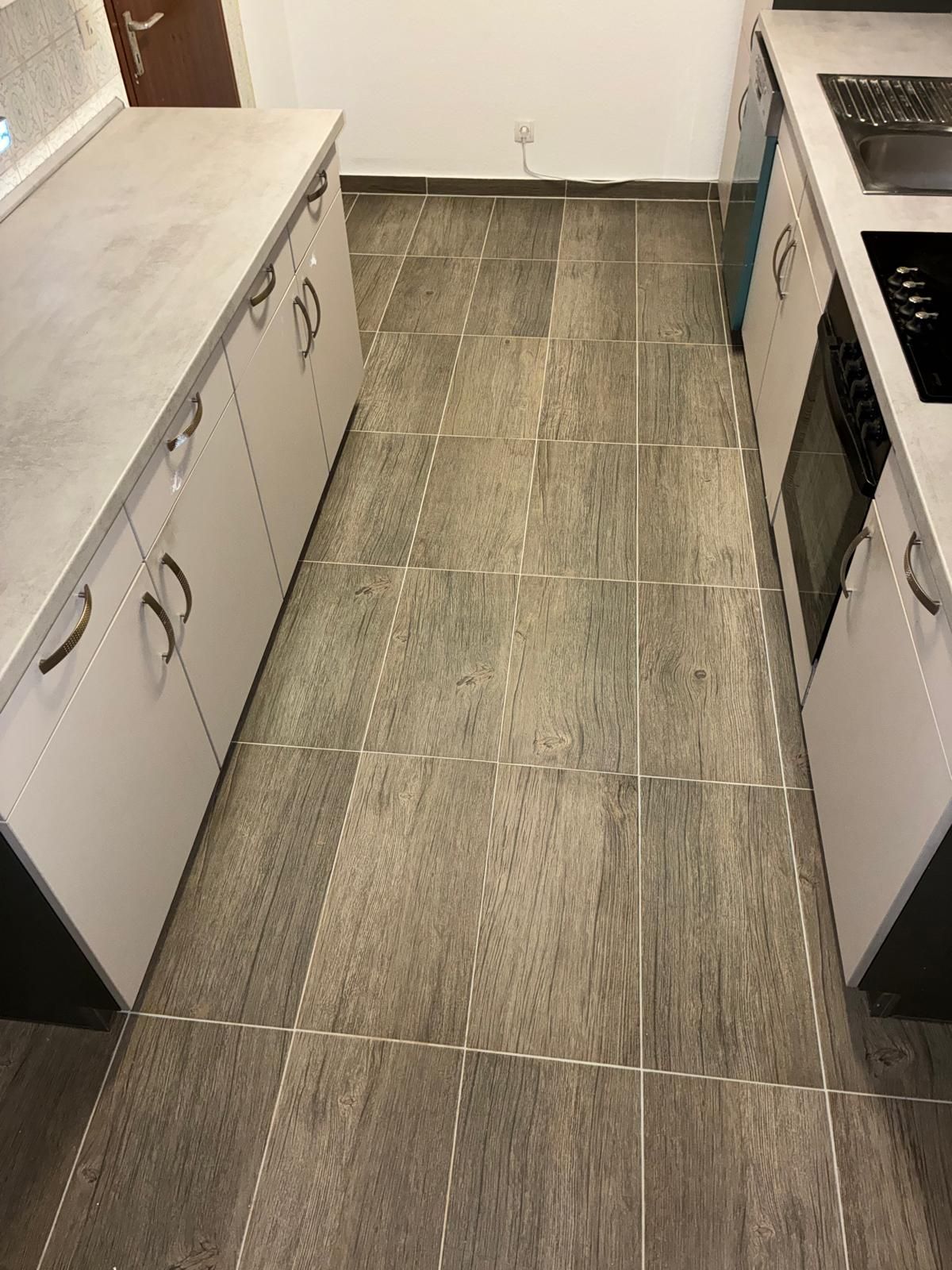 Kitchen with gray wood-look tile floor. White cabinets with silver handles line both sides. A stovetop and oven are visible.