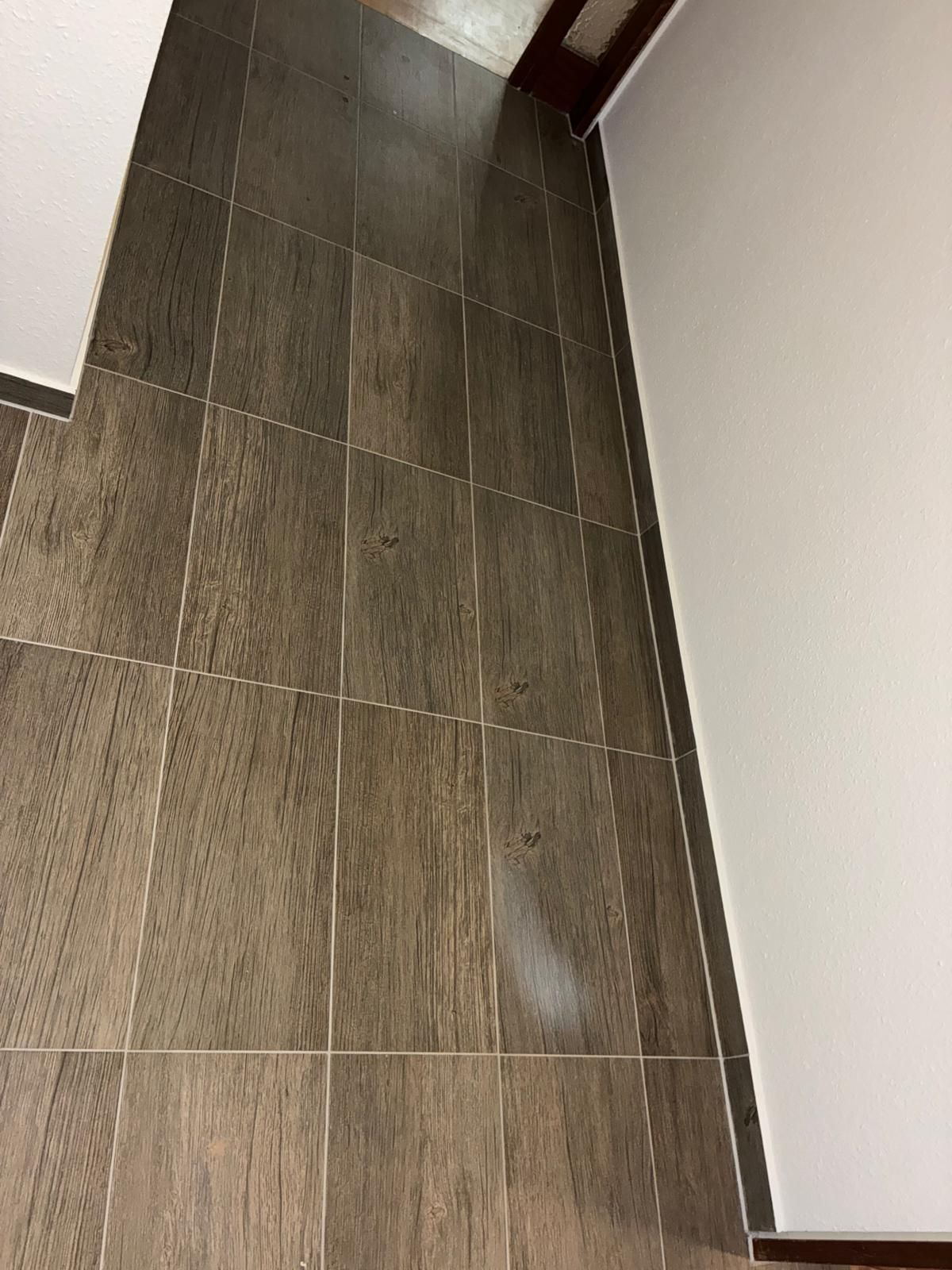 Brown wood-look tile floor next to a white wall and a light-colored top corner.