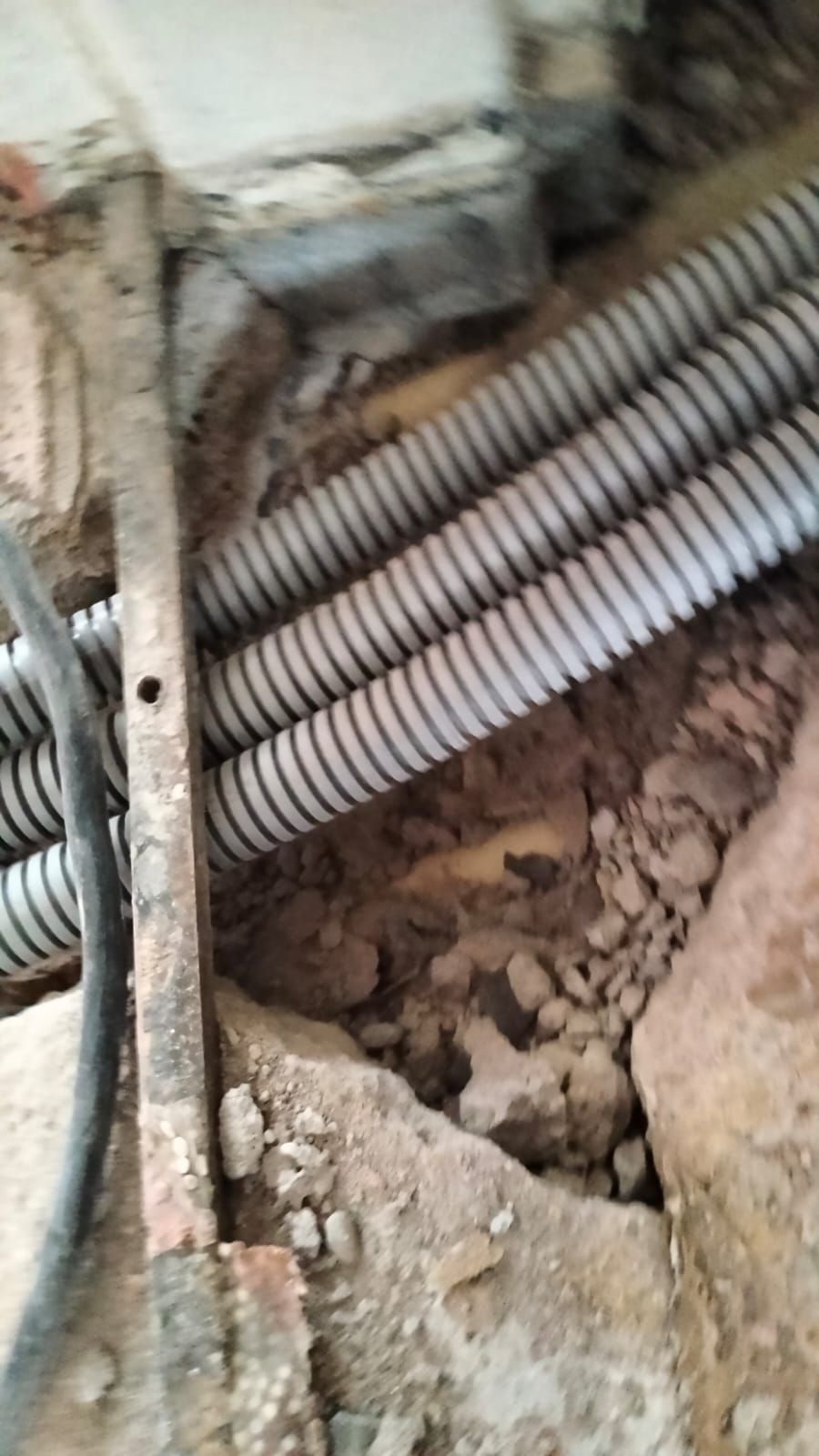 Electrical conduits in a recessed area with exposed dirt and a metal support beam.