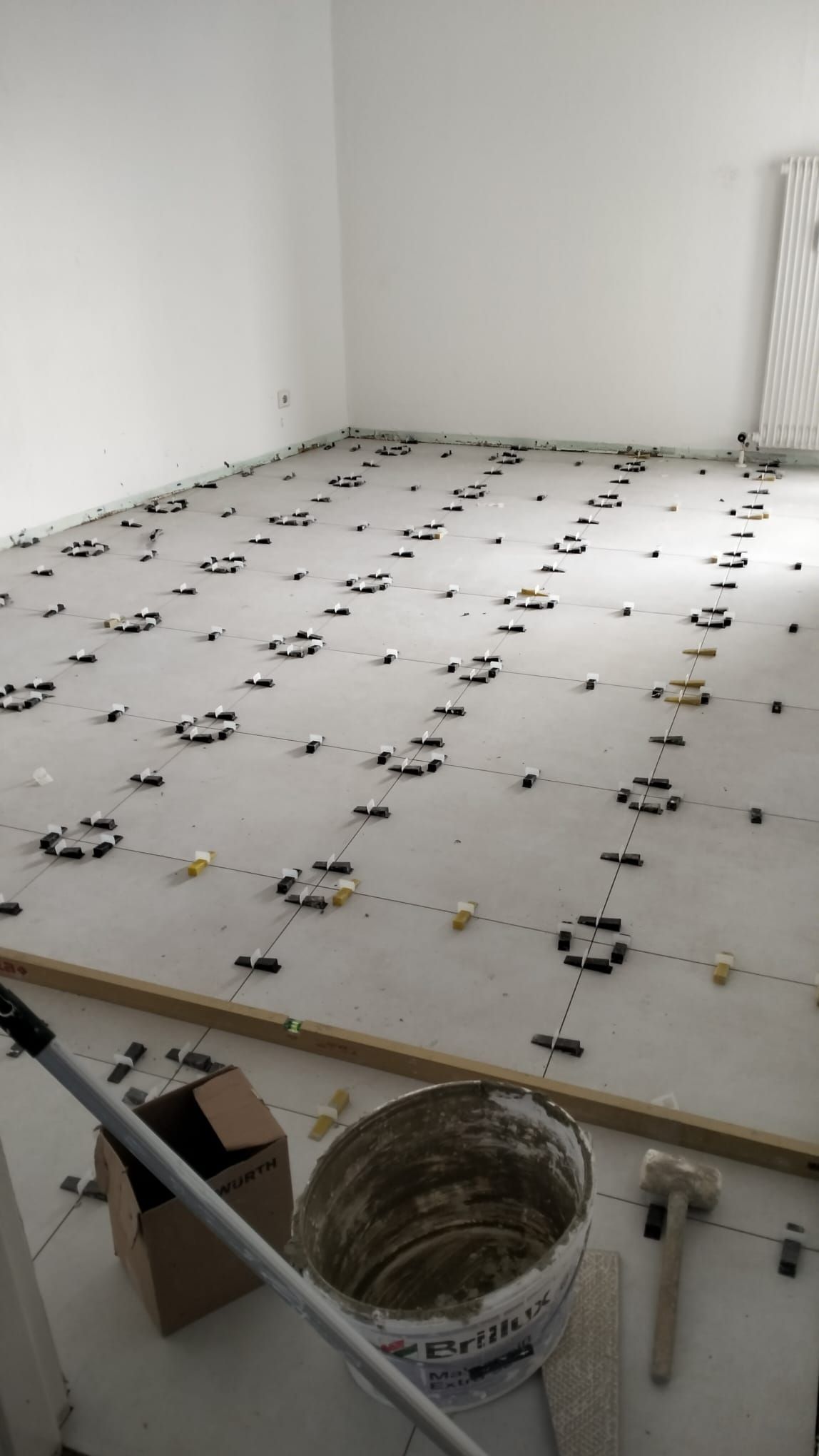 Room with floor tiling under installation. Tiles are spaced with leveling systems.