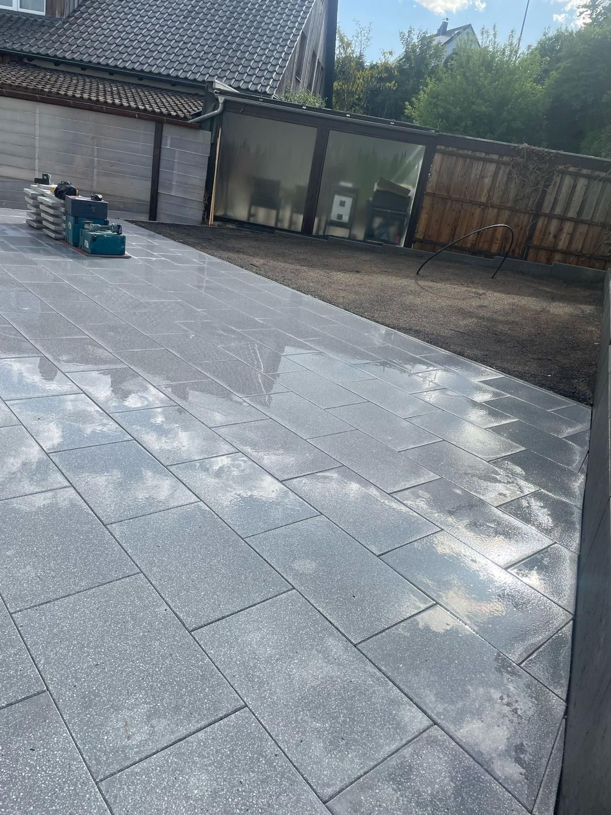 Gray paved patio with a shed and construction materials.