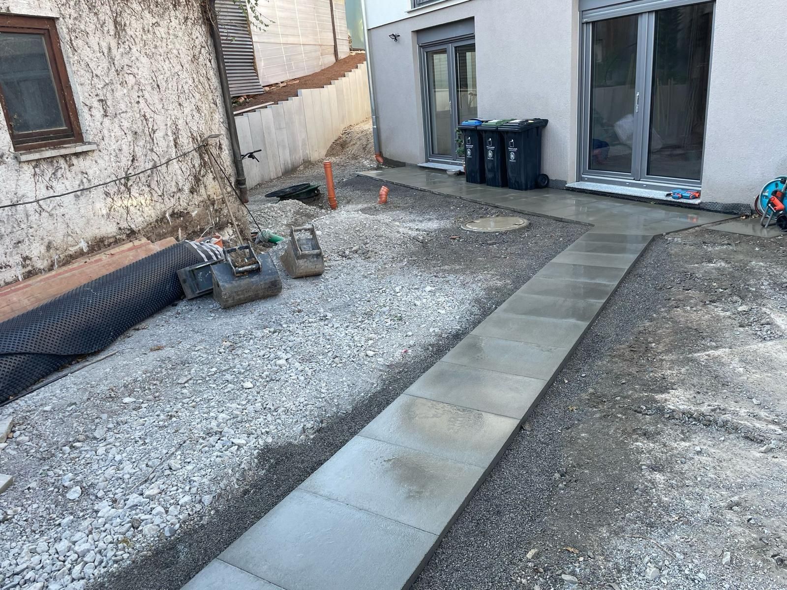 A paved walkway being constructed through a gravel-covered construction site between two buildings.