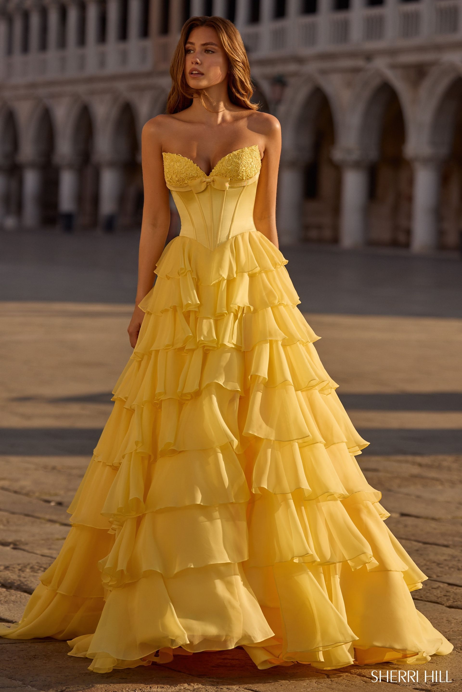 Woman in yellow strapless gown, adorned with ruffles and bodice details, posing outdoors.