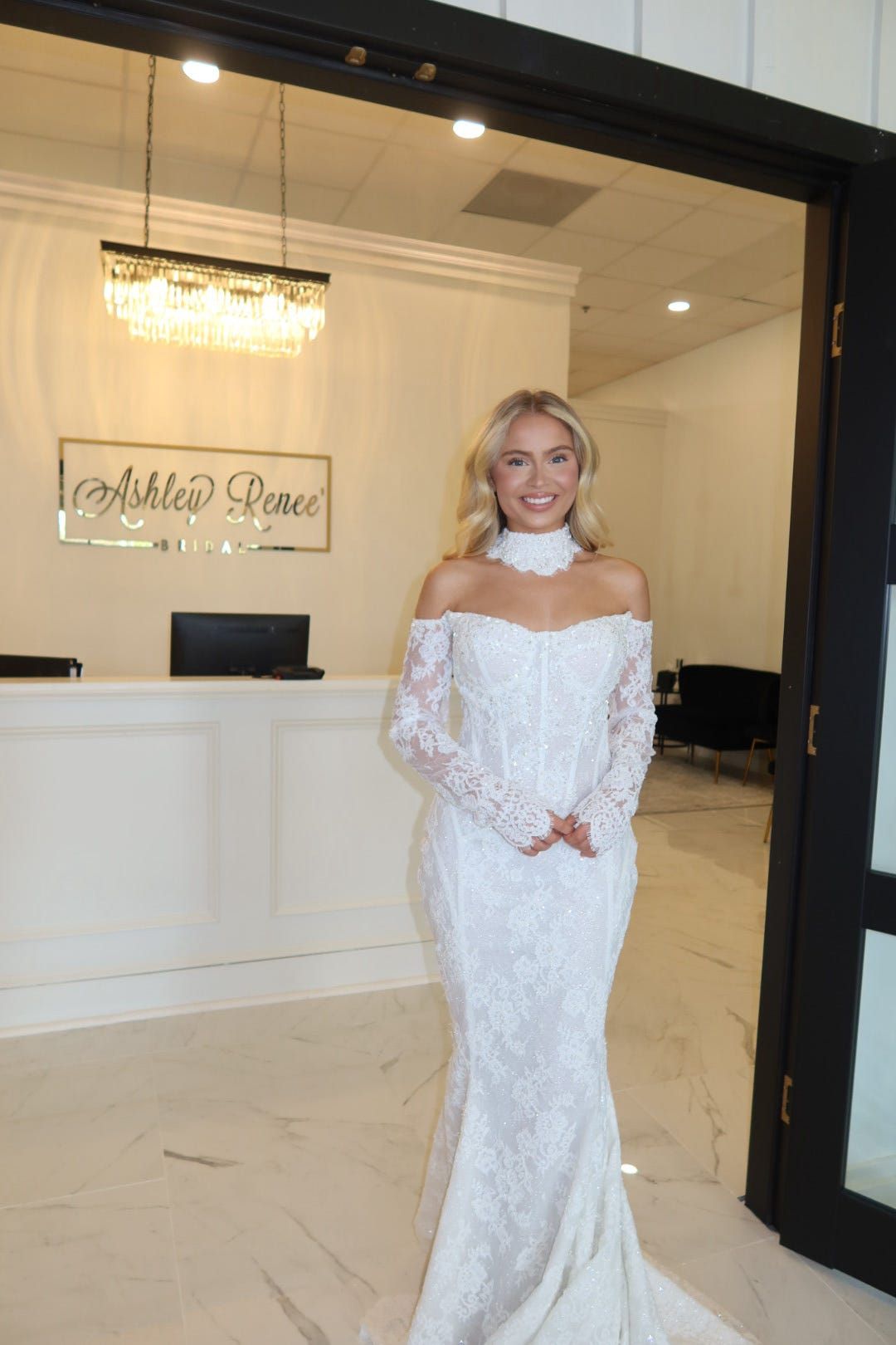 A woman in a white lace dress is standing in front of a door.