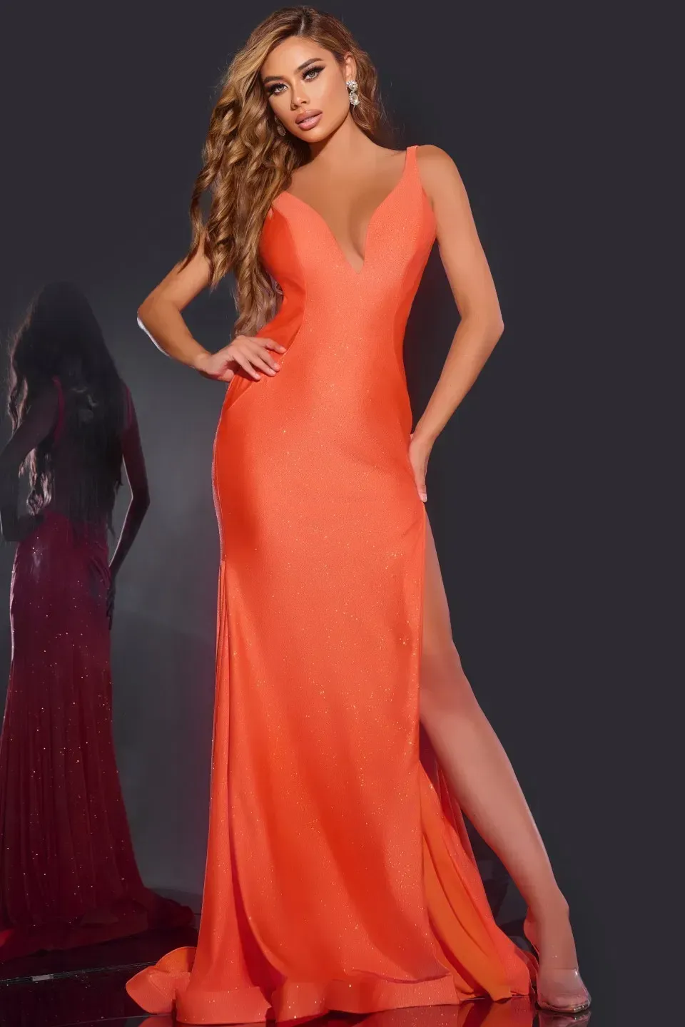 Woman in orange gown with a high slit, posing in a studio.