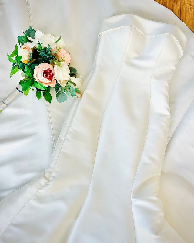 A bouquet of flowers is sitting on top of a white wedding dress.
