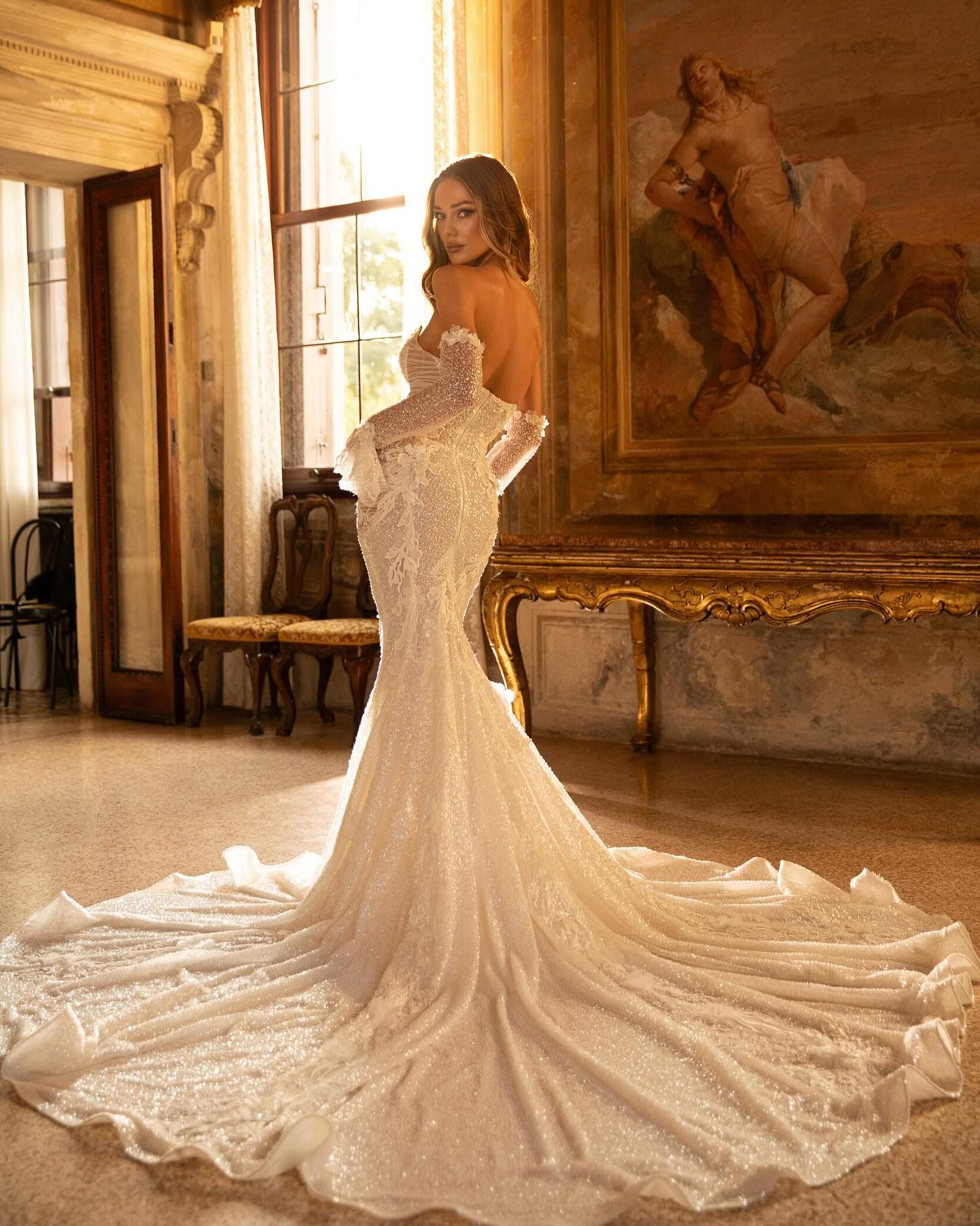 A woman in a wedding dress is standing in a room in front of a painting.