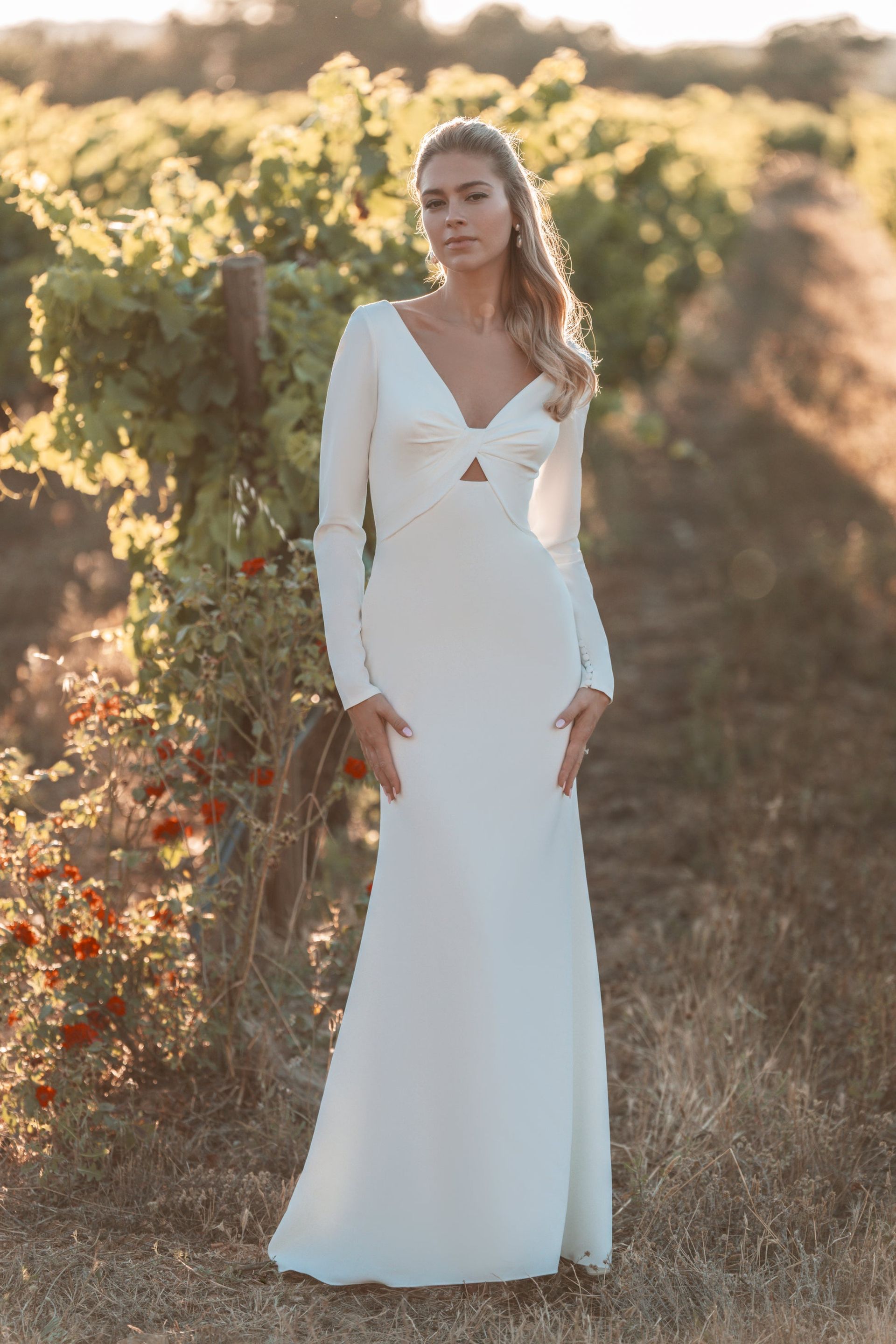 A woman in a white wedding dress is standing in a vineyard.