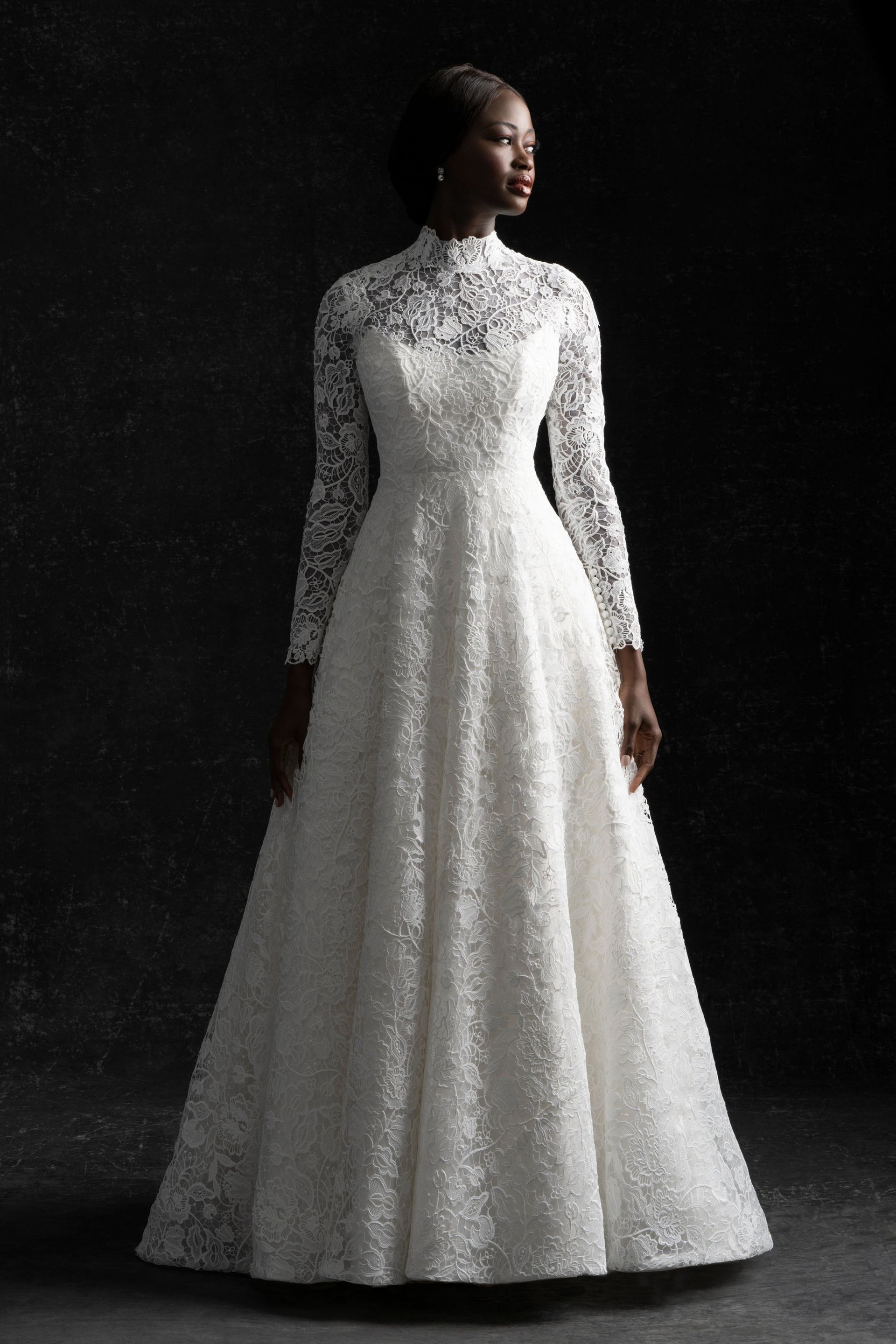 A woman is wearing a white lace wedding dress with long sleeves.