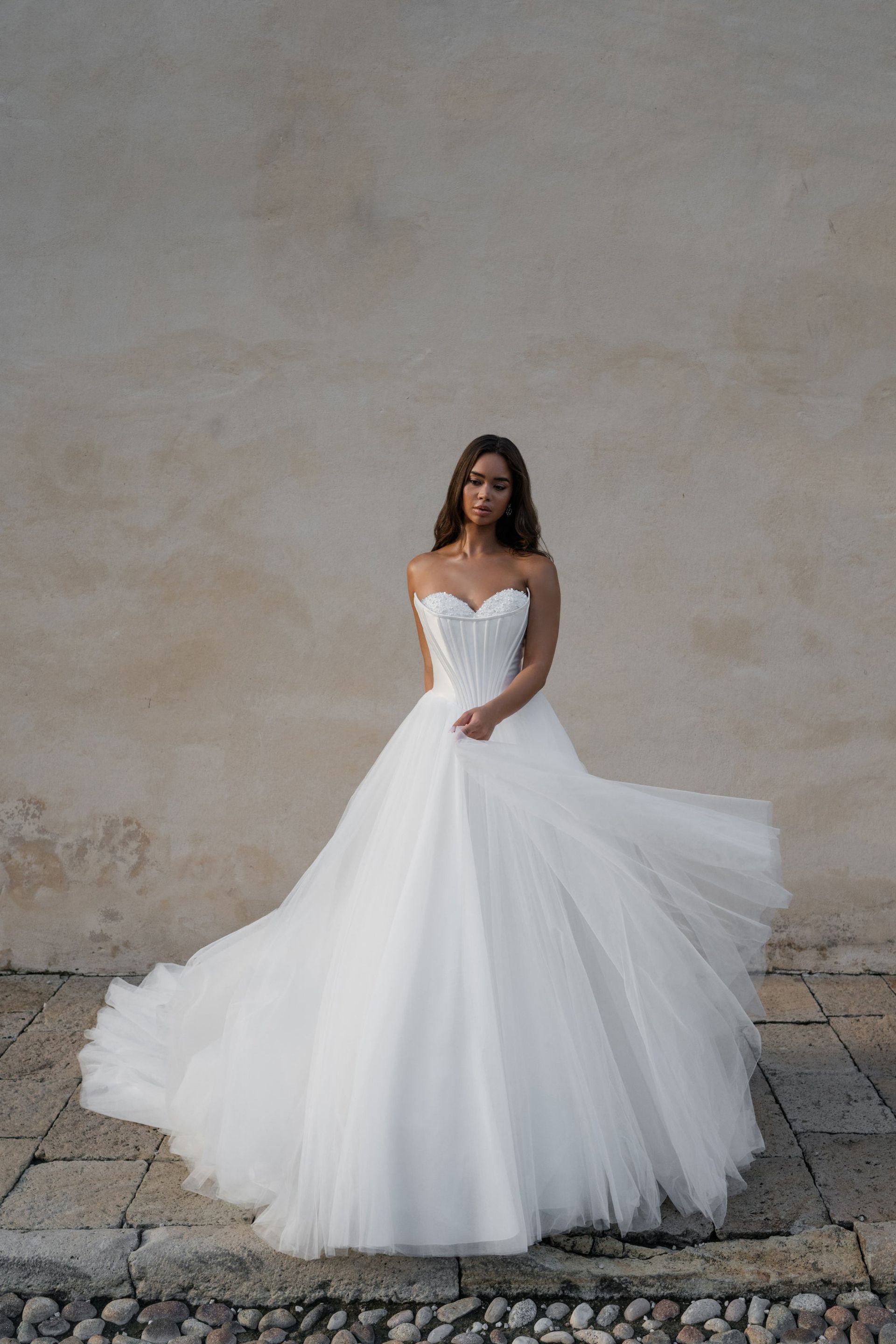 A woman in a white wedding dress is standing in front of a wall.