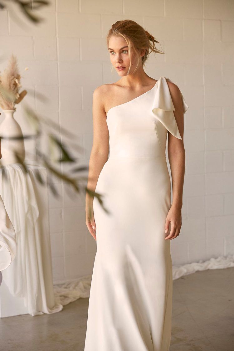 A woman in a white one shoulder wedding dress is standing in a room.