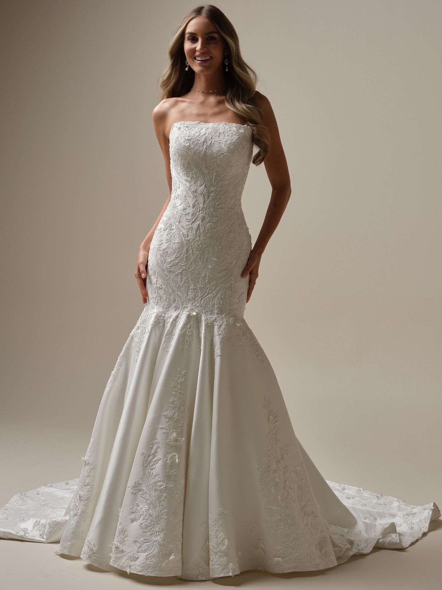 Woman in a strapless, beaded mermaid wedding dress smiles, set against a neutral background.
