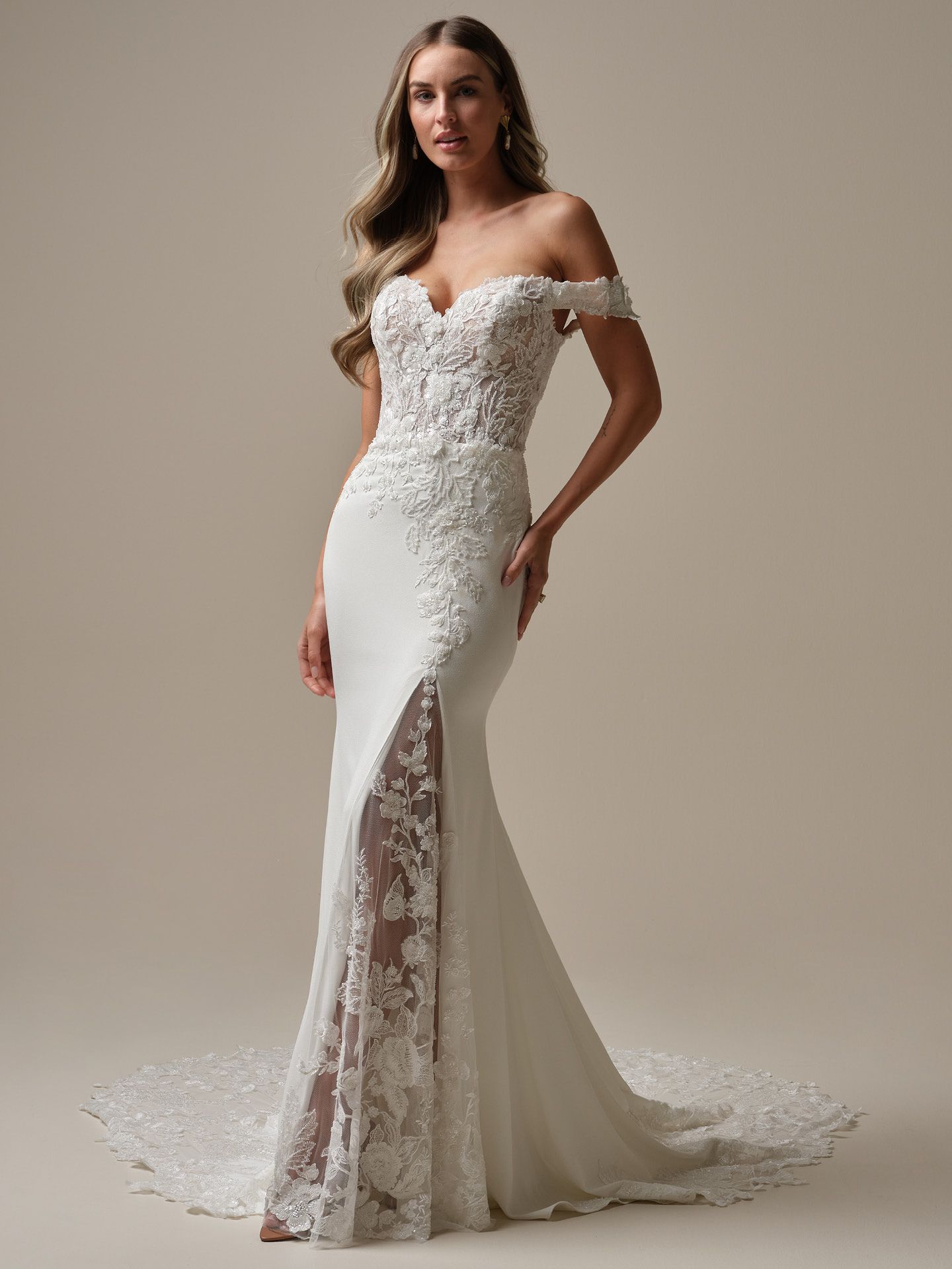 Woman in white off-shoulder wedding dress with lace side panel, train, and long wavy hair.