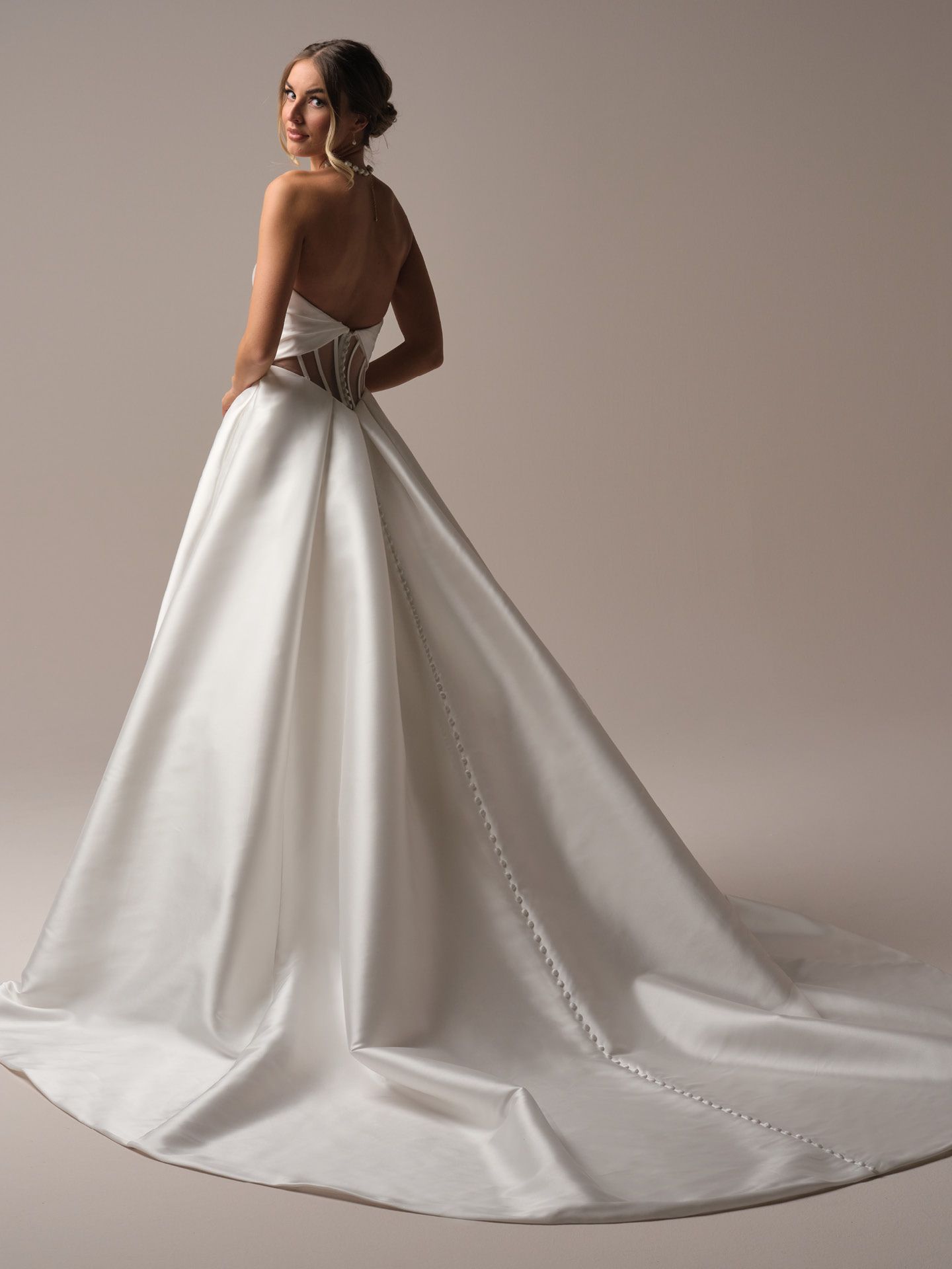 Woman in white strapless wedding gown with train, looking over shoulder.
