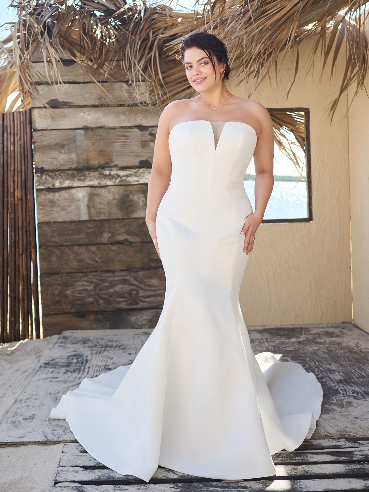 A woman in a white wedding dress is standing in front of a wooden building.