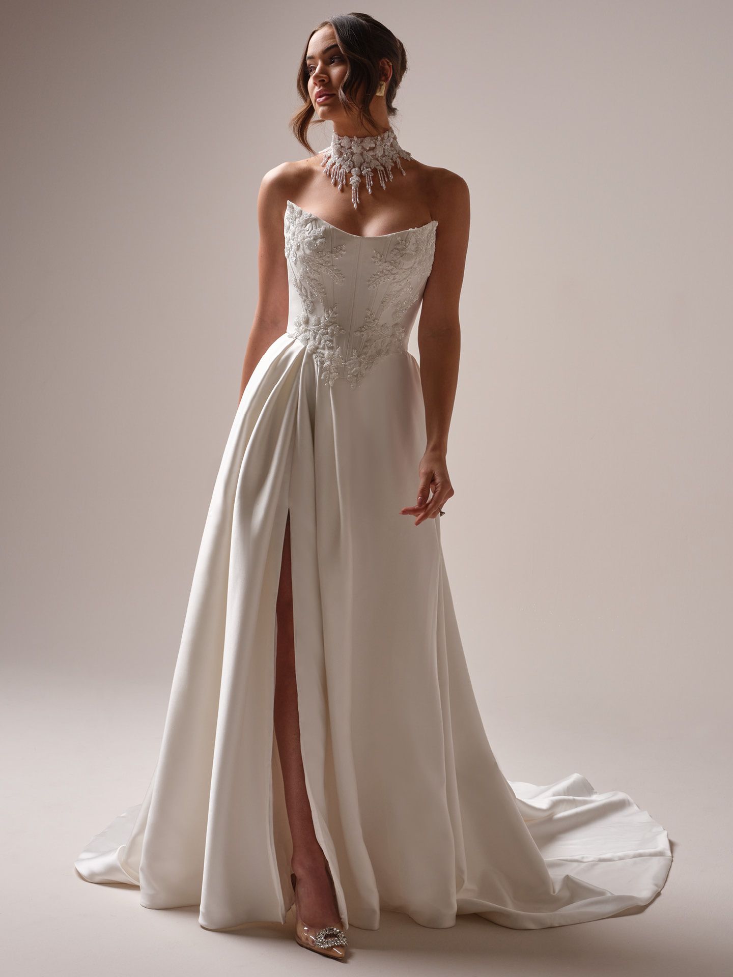 Woman in a white wedding dress with a high slit, embellished bodice, and choker necklace.