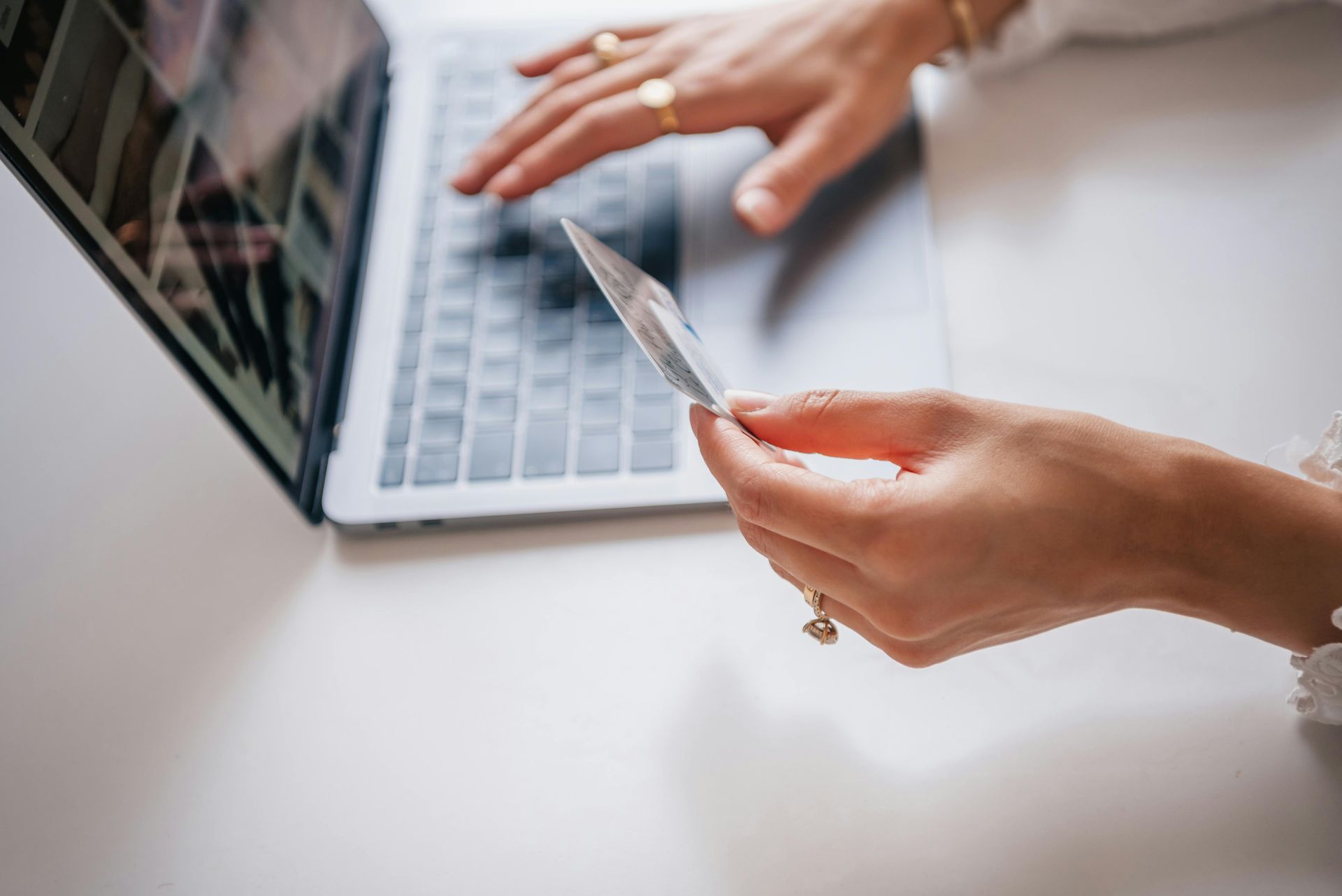 A woman is holding a credit card in front of a laptop computer.