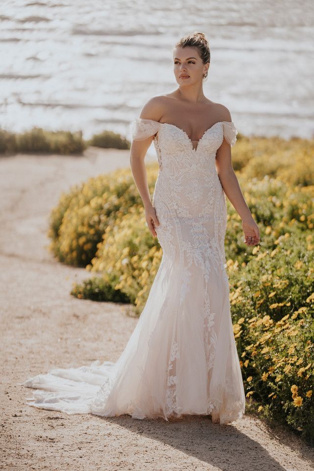 A woman in a wedding dress is standing in front of a body of water.