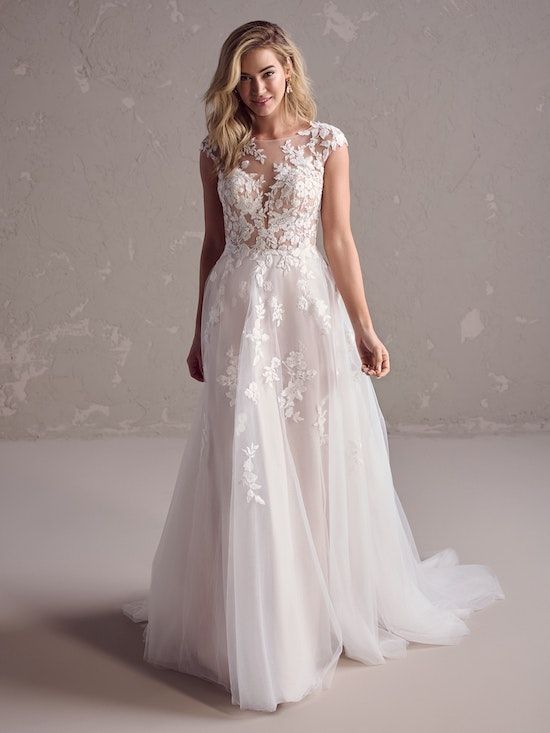 A woman in a white wedding dress is standing in front of a wall.