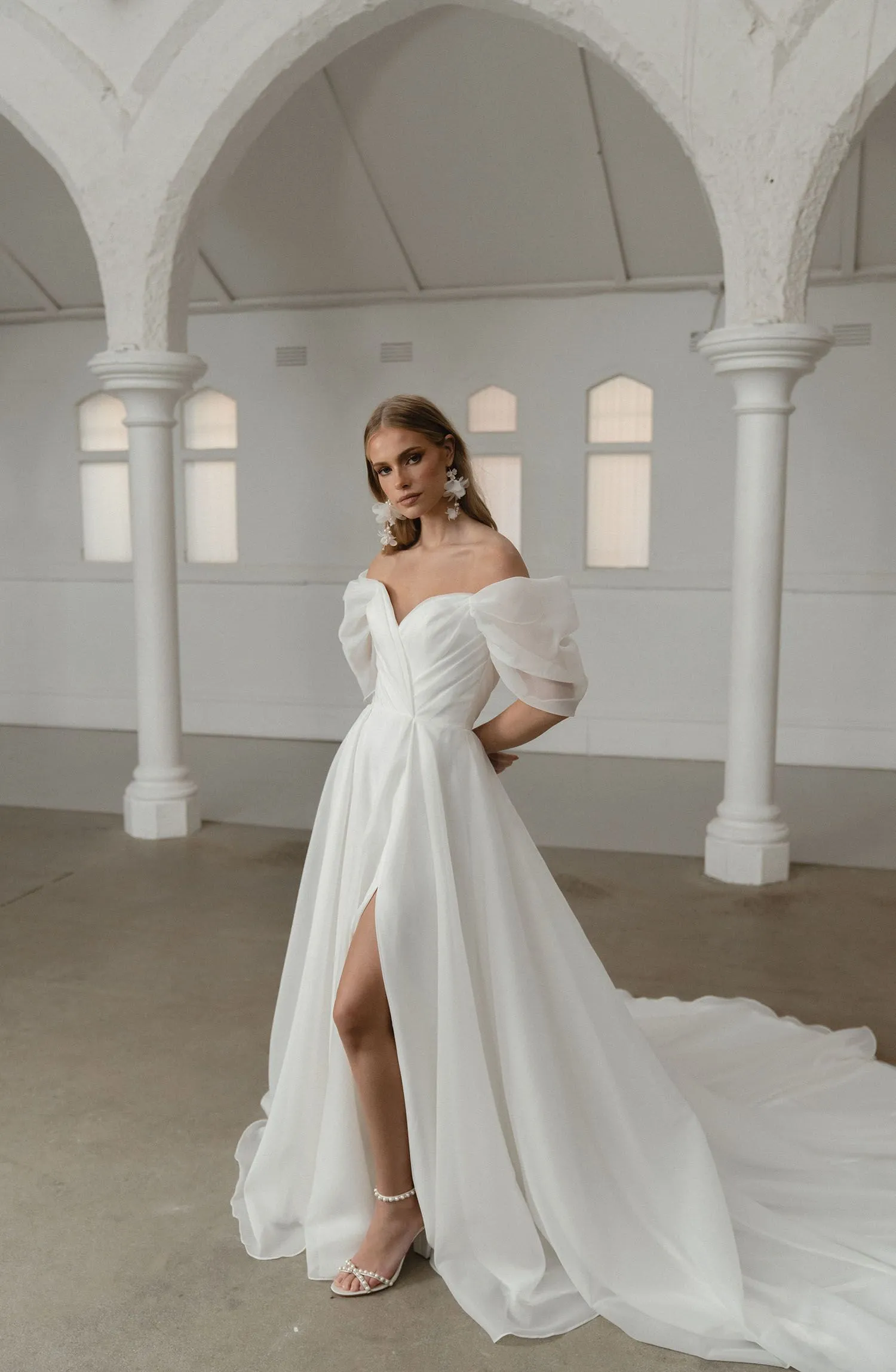 A woman in a white wedding dress is standing in a room with arches.