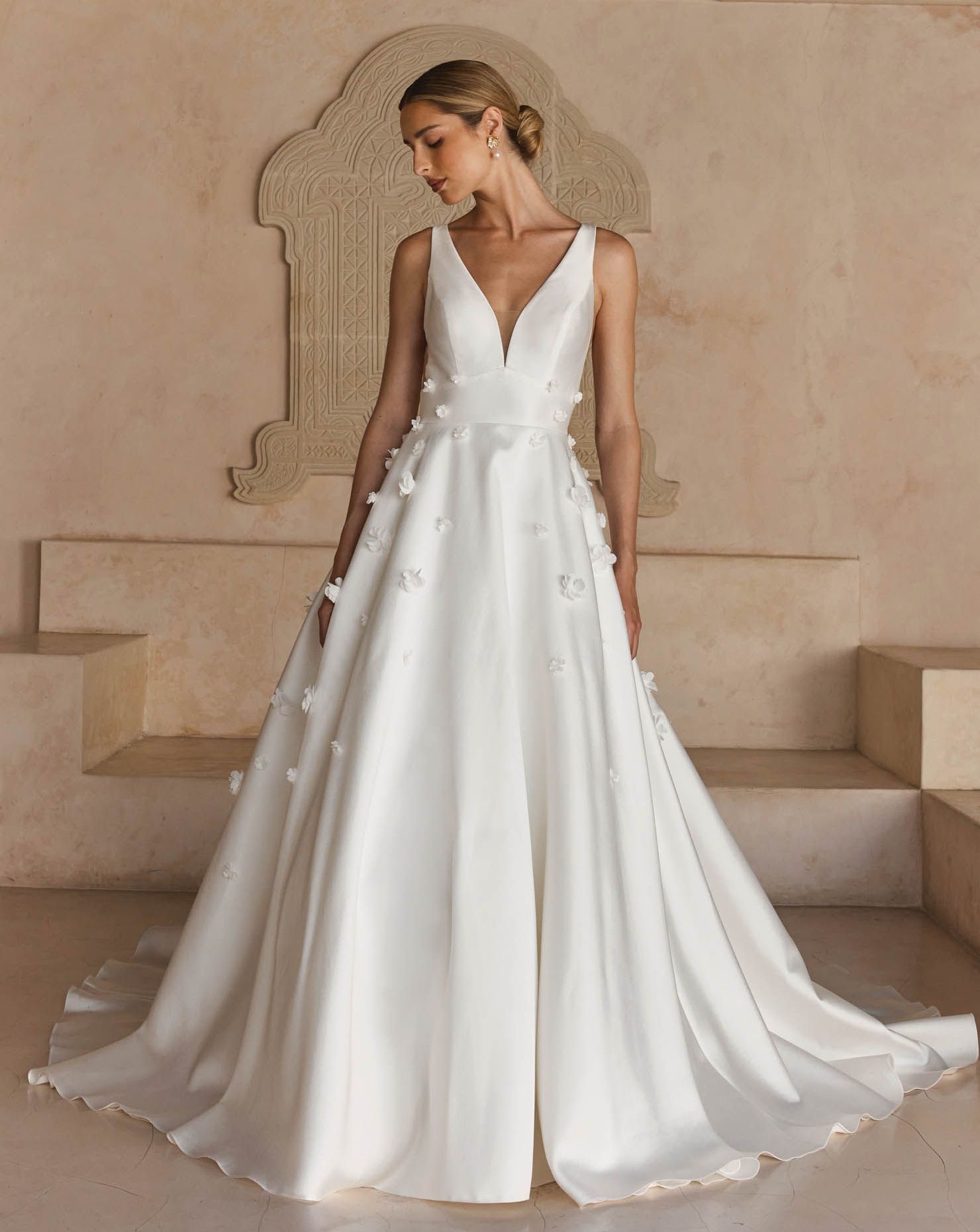 A woman in a white wedding dress is standing in front of a wall.
