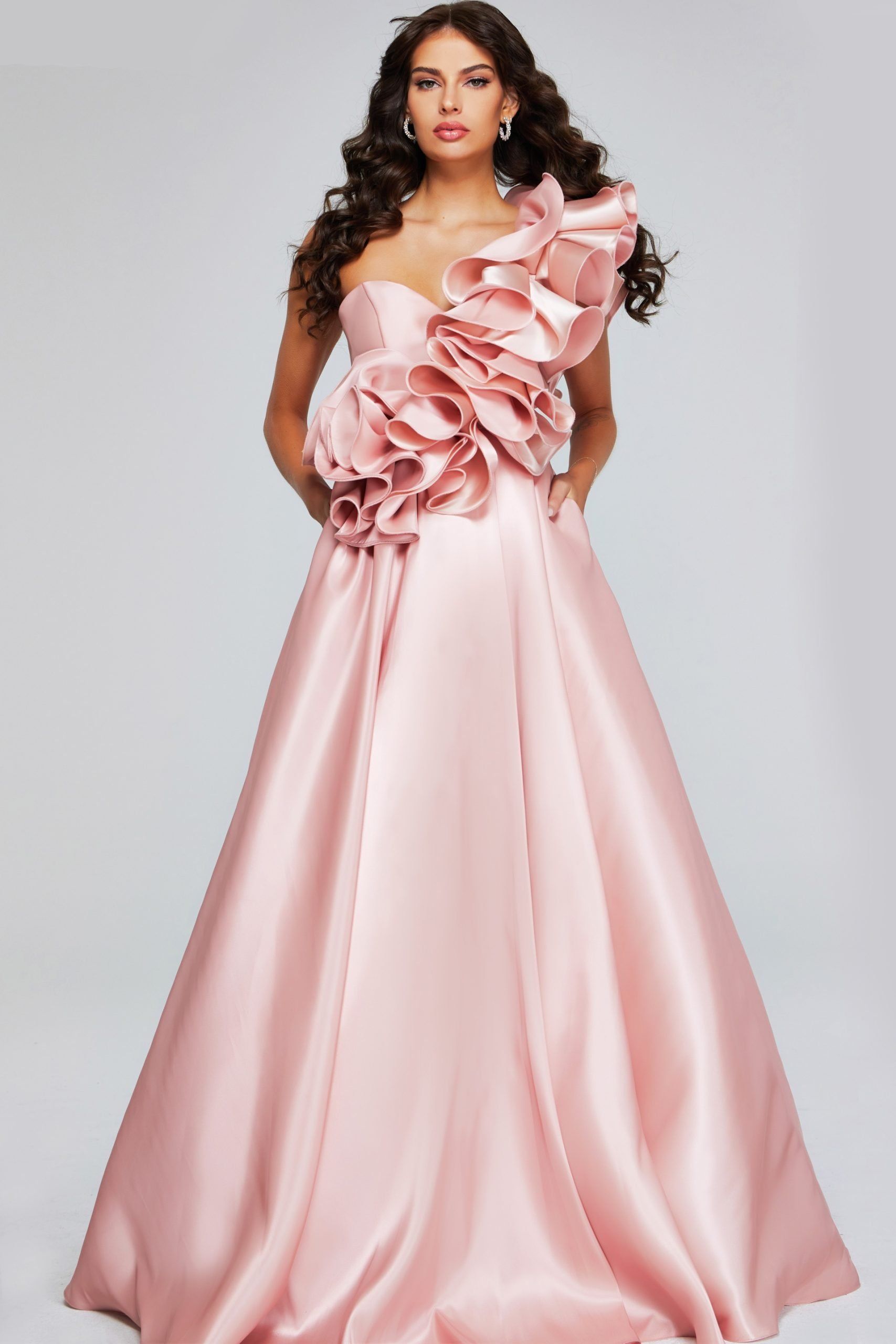 A woman is wearing a long pink dress with ruffles on the shoulder.