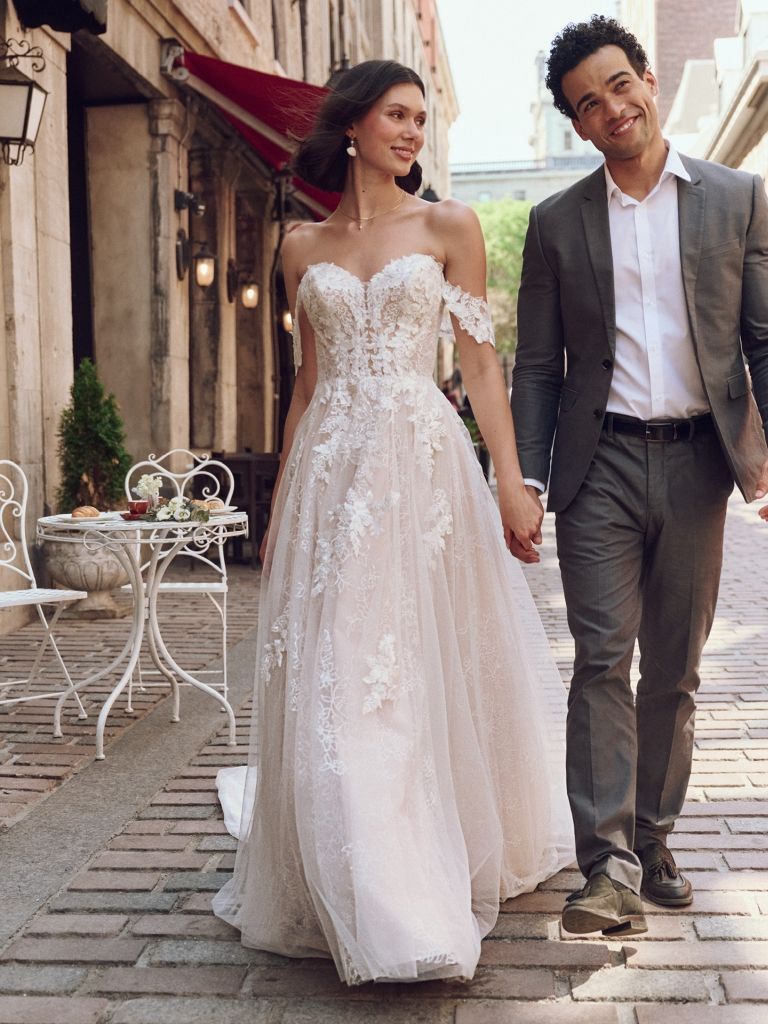 A bride and groom are walking down a cobblestone street holding hands.