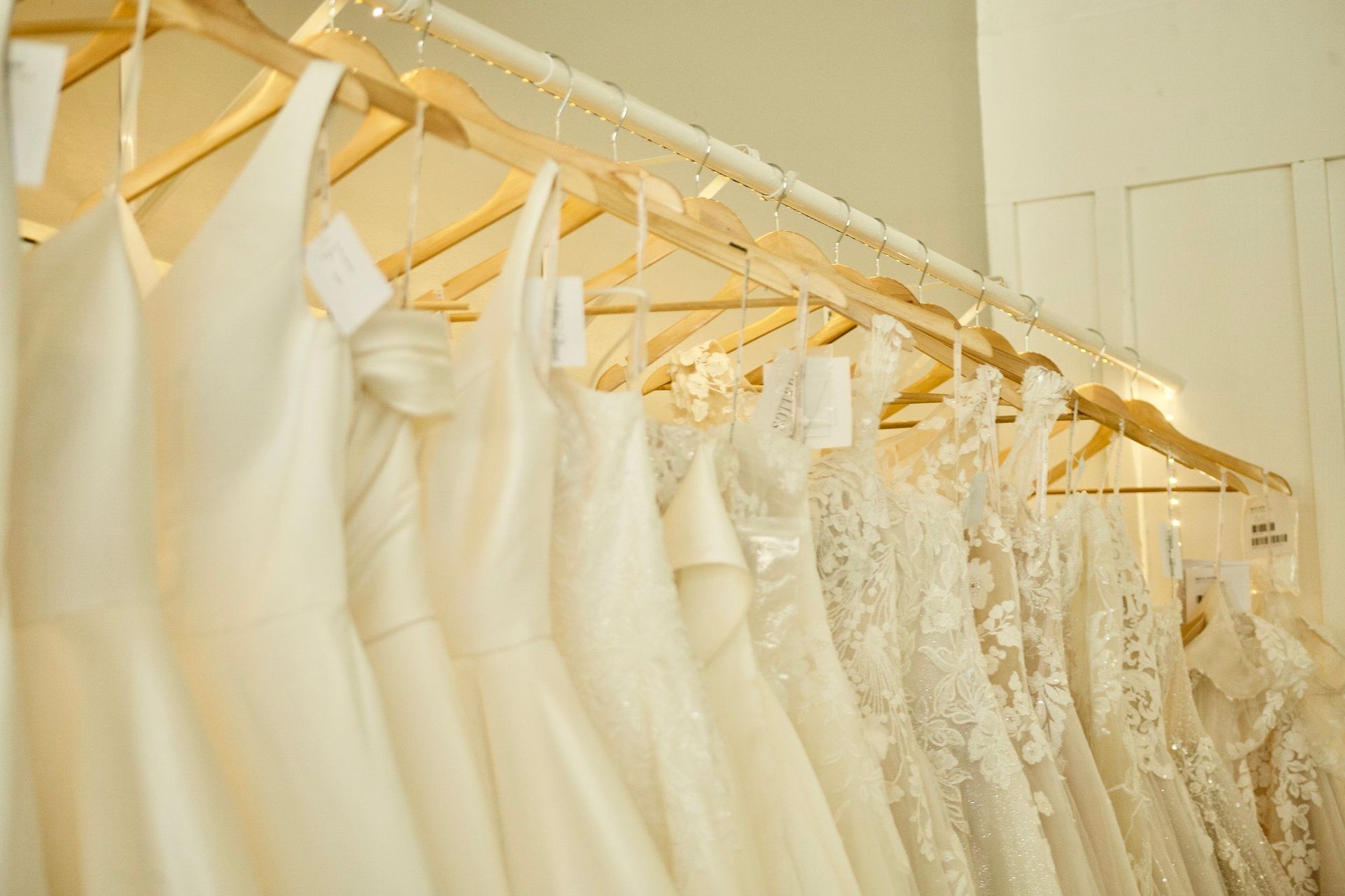 A row of white wedding dresses hanging on wooden hangers in a store.
